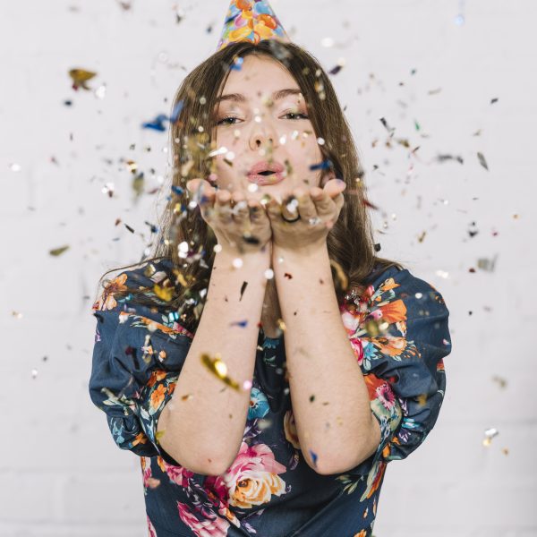 teenage girl blowing confetti from hand against white backdrop